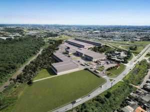 Vista aérea de um galpão logístico em Curitiba, com vários módulos industriais, pátios de manobra de caminhões e acesso pela rodovia, cercado por áreas verdes e pela malha urbana ao fundo. Excelente para solução logística.