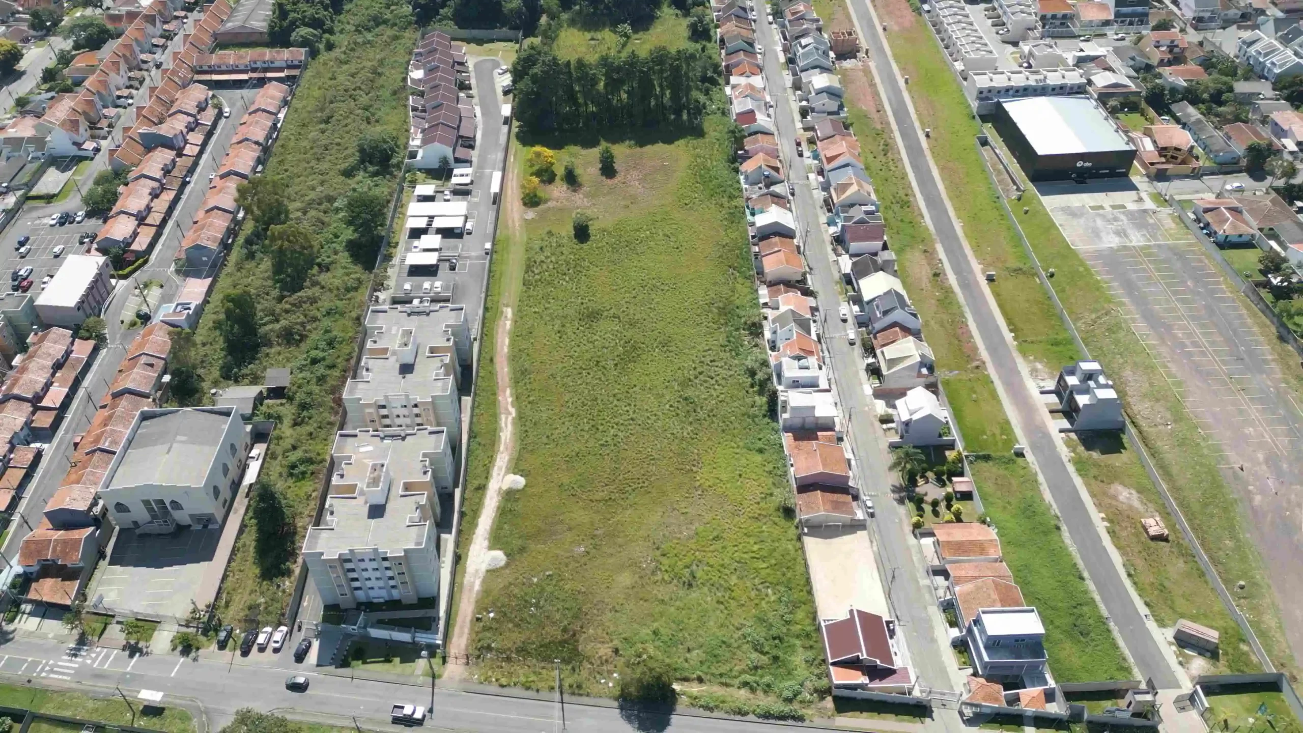 Vista aérea de um lote vazio cercado por casas e prédios residenciais, destacando oportunidades de lotes à venda em Curitiba.